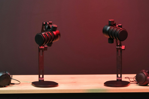 2 microphones and 2 headphones on a table with a red light shining down on them.