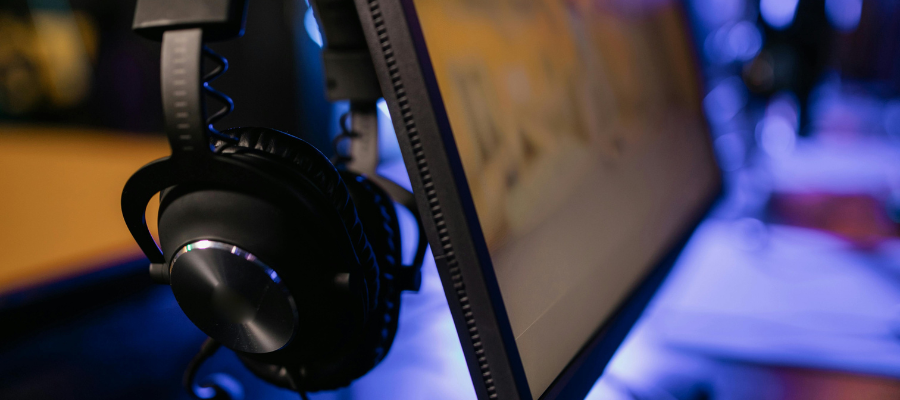 A close-up photo of a monitor and headphones with purple light in the background.