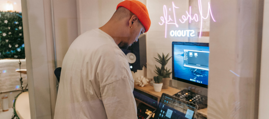 Someone editing a podcast with a orange beanie and white long-sleeve shirt on